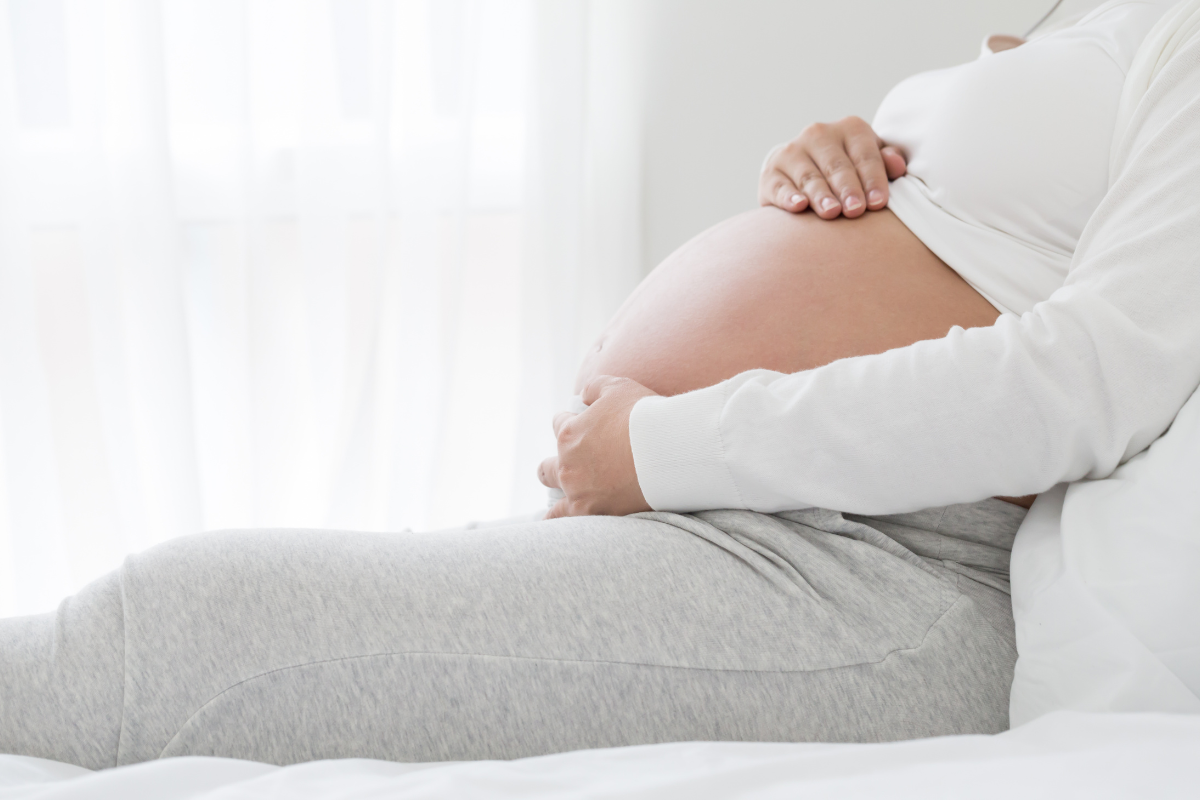 Pregnant woman resting on a bed, cradling her belly in a calm & serene environment