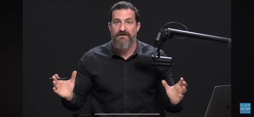Bearded presenter speaking into a studio podcast microphone against a dark backdrop.