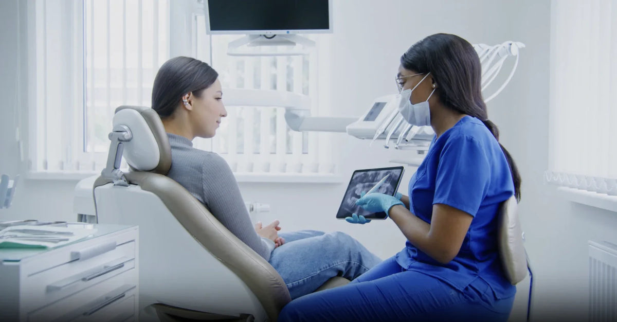 Dentist in blue scrubs shows a patient dental X-rays on a tablet during a checkup.