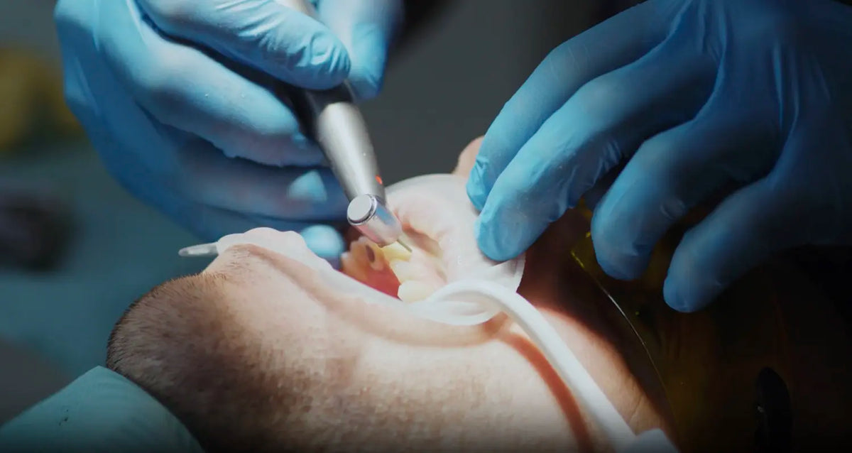 Dentist in blue gloves cleans a patient's teeth to remove plaque buildup.
