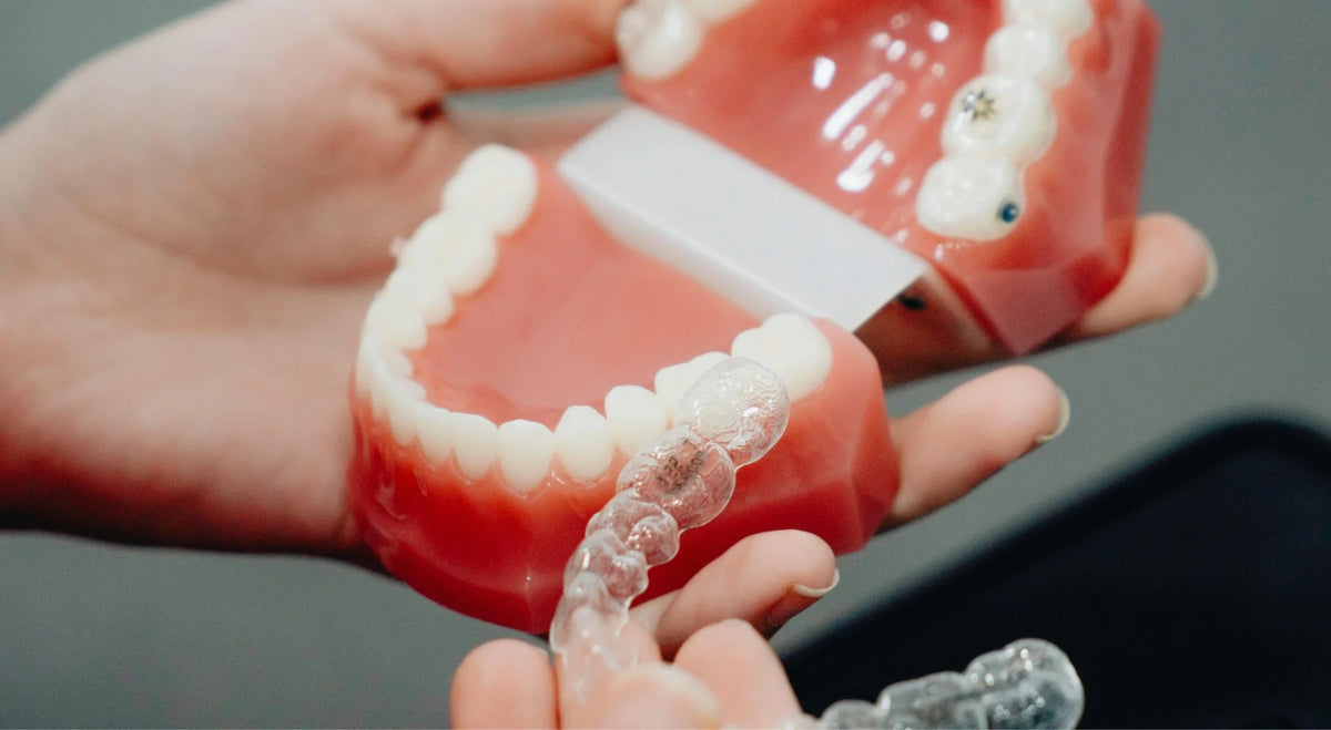 Hands holding a dental jaw model with braces beside a clear plastic retainer.