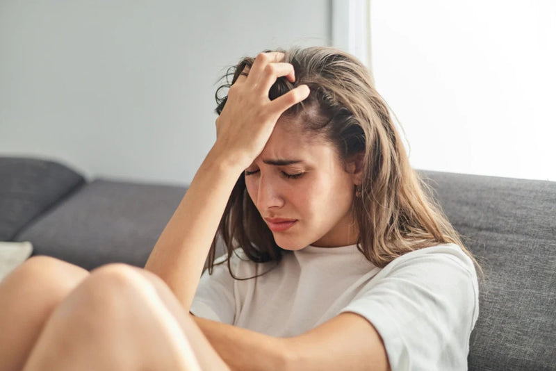 Distressed person sitting on a couch holding their head, illustrating anxiety and depression.