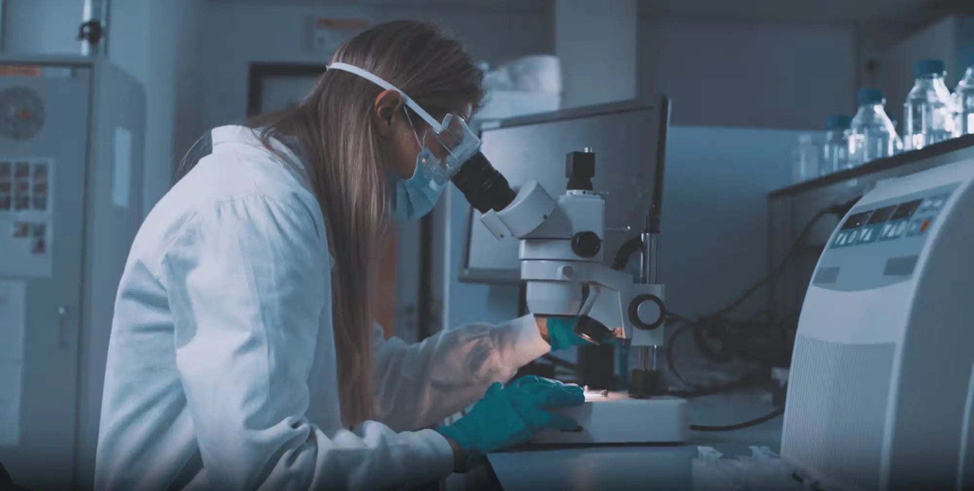 Scientist wearing protective gear & examining samples under a microscope in a laboratory setting