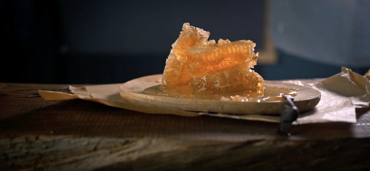 Golden honeycomb pieces oozing raw honey on a wooden board over rustic table.