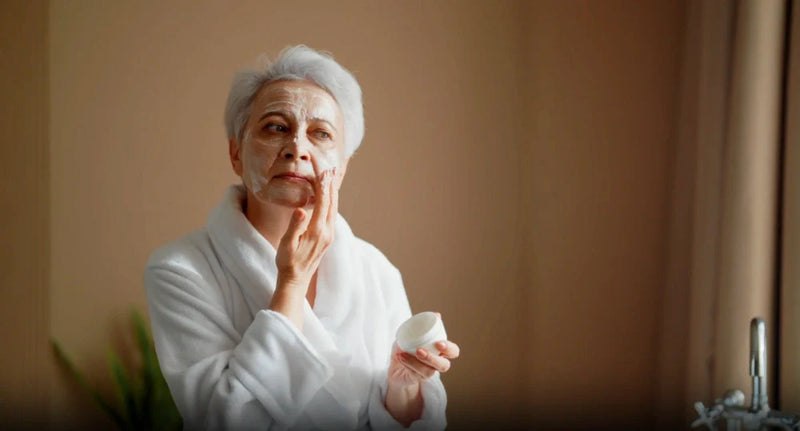 Person in white robe applying face cream from a jar, illustrating skincare after 40.