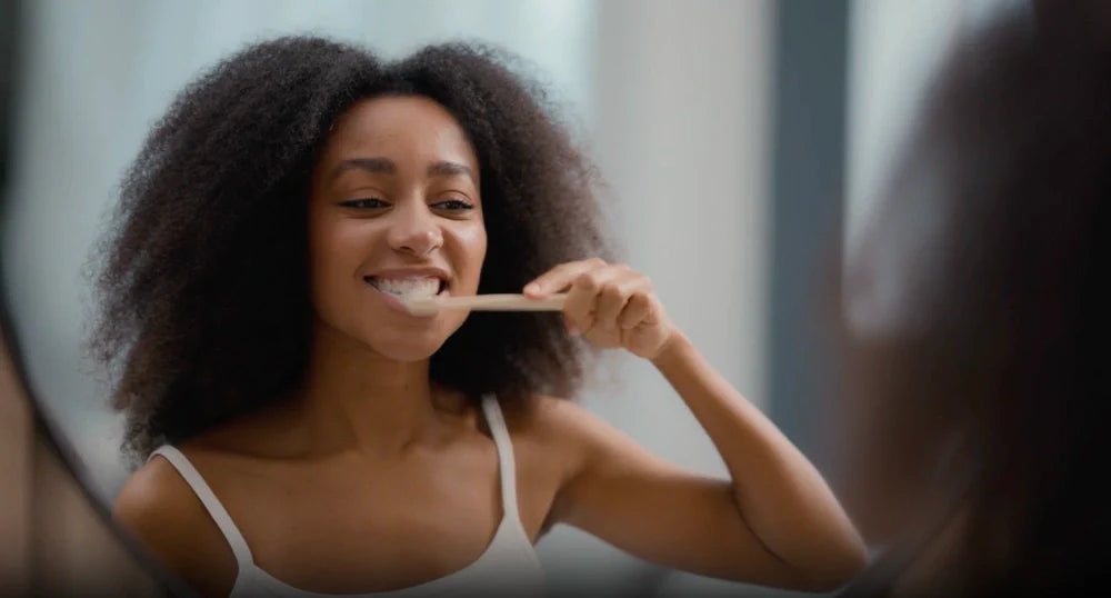 Person brushing teeth in a bathroom mirror as part of an evening oral care routine.