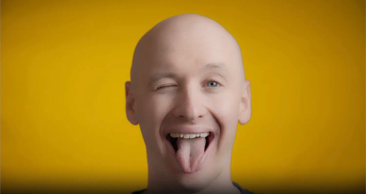 Winking person sticking out tongue against a yellow background, illustrating tongue cleaning for fresh breath.