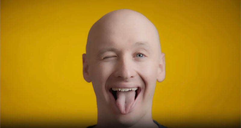 Winking person sticking out tongue against a yellow background, illustrating tongue cleaning for fresh breath.