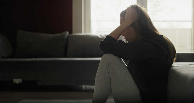 Person sits on floor by a couch, head in hand, illustrating anxiety and depression.