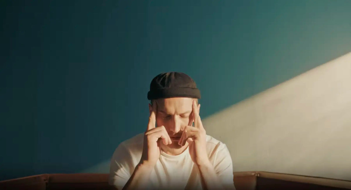 Person in a black beanie pressing fingers to temples, eyes closed with brain fog.