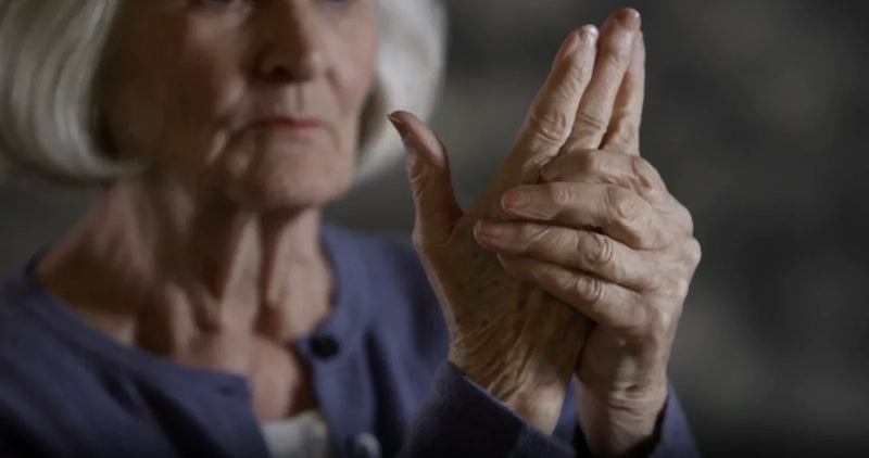 Older person massaging arthritic hand joints, illustrating the link between arthritis and oral health.