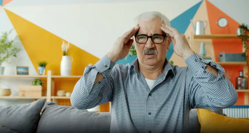 Older person pressing both temples, illustrating memory loss connected to poor oral health.