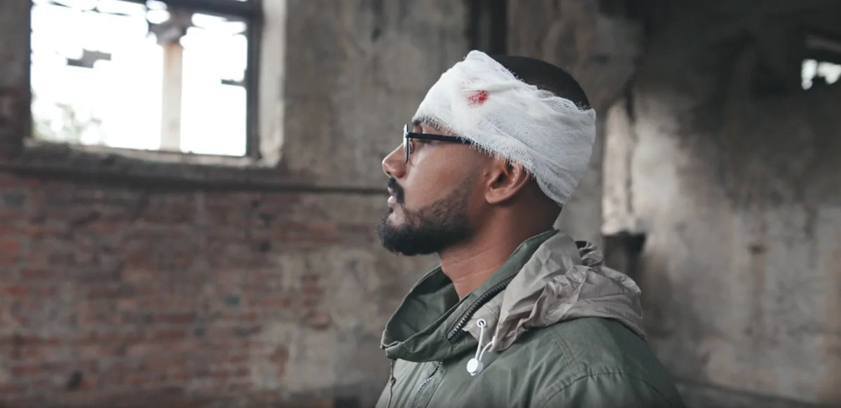 Person with a blood-stained head bandage stands in a derelict brick building, illustrating traumatic brain injury.