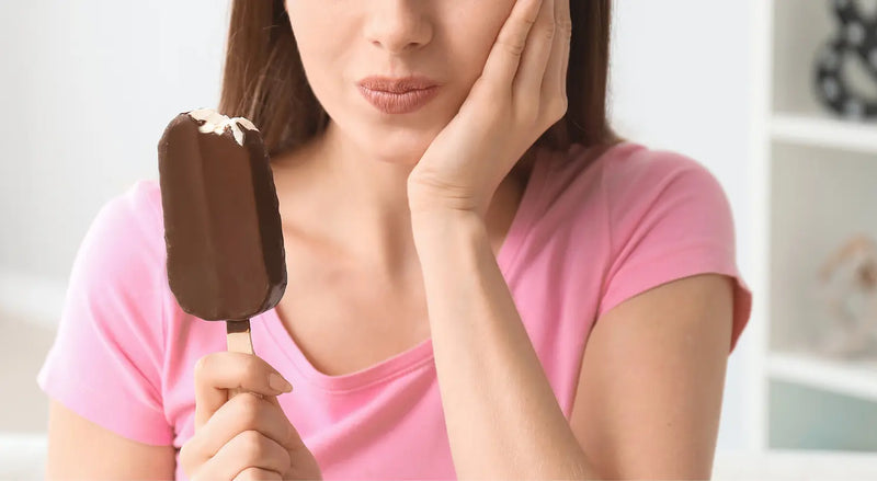 Person holding a chocolate ice cream bar while wincing from tooth sensitivity pain.