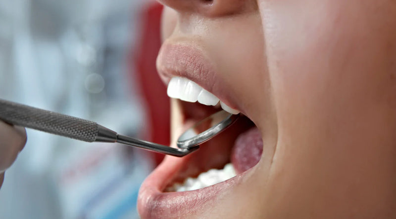 Dental mirror examining an open mouth during a routine oral health checkup close-up.