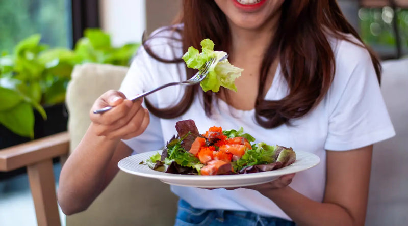 Person eating a fresh salmon and mixed greens salad, forkful of lettuce raised to mouth.