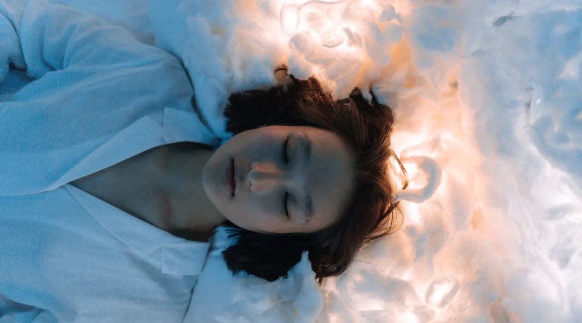 Person sleeping peacefully on soft white bedding bathed in warm and cool light.