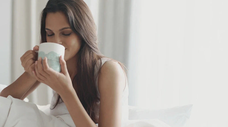 Person sipping morning coffee in bed, illustrating how coffee can stain teeth over time.