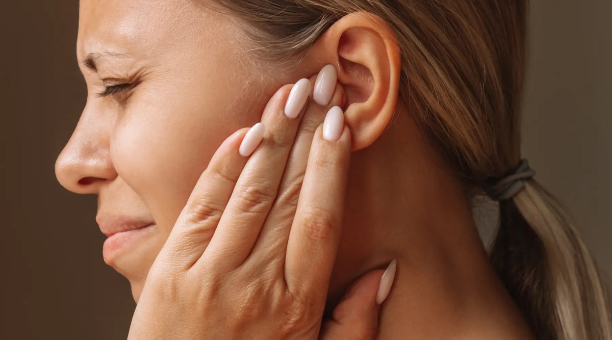 Person wincing while holding their ear and jaw, showing pain from a spreading tooth infection.