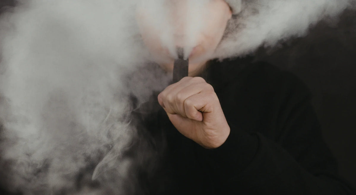 Person exhaling a thick cloud of vapor while holding a vape device.