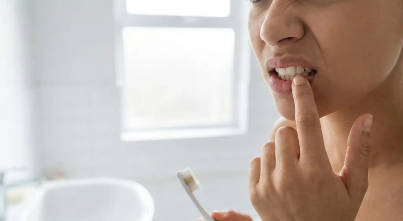 Person checking their gums in a bright bathroom while holding a toothbrush.