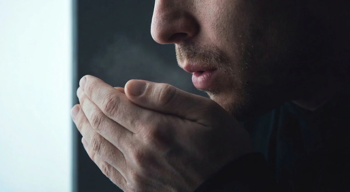 Close-up profile of a person breathing into cupped hands to check breath.
