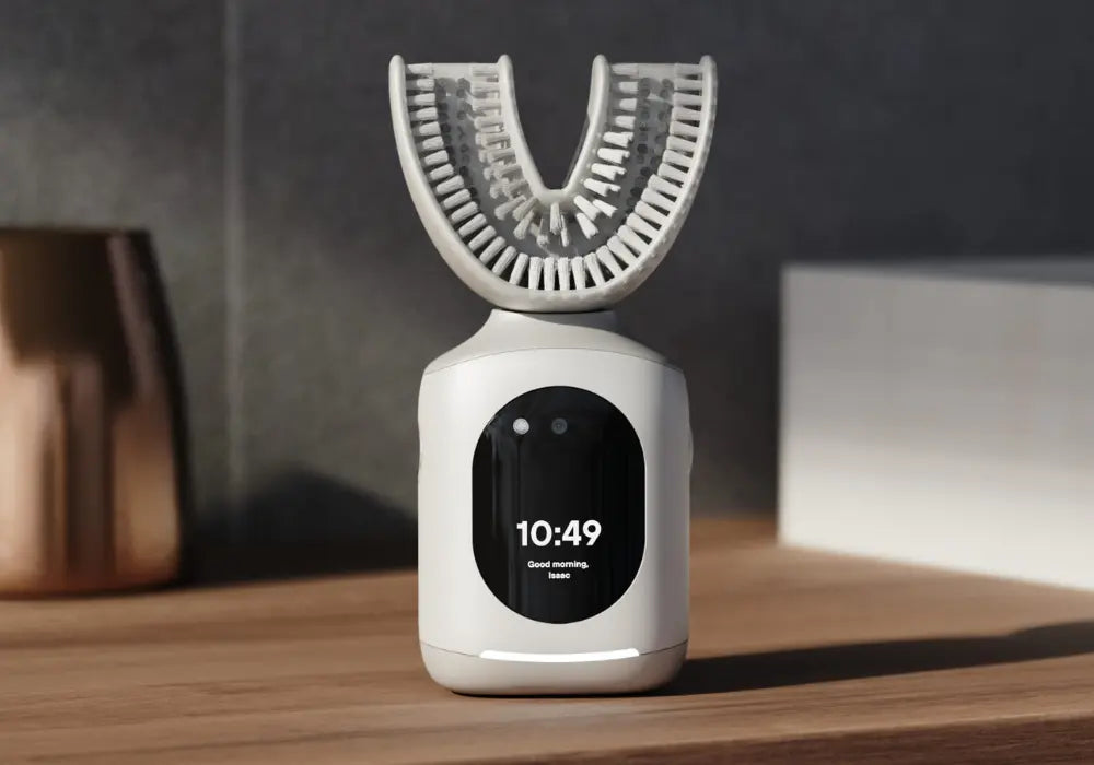 Hands-free toothbrush resting on a bathroom counter with a digital clock and personalized greeting on screen