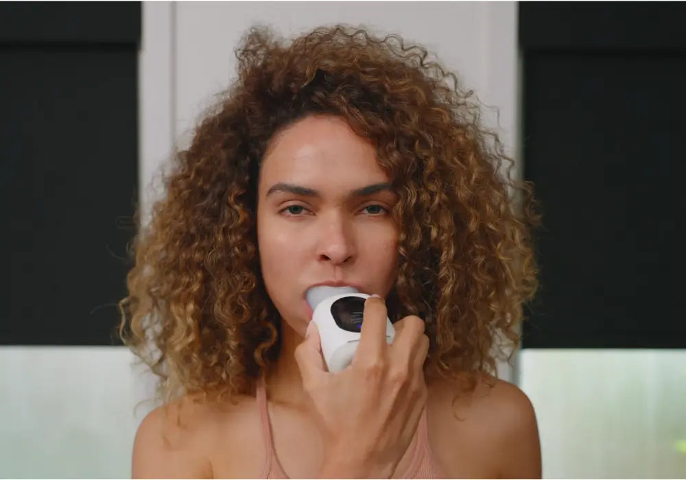 Person cleaning teeth with a white U-shaped smart toothbrush mouthpiece in a bathroom.